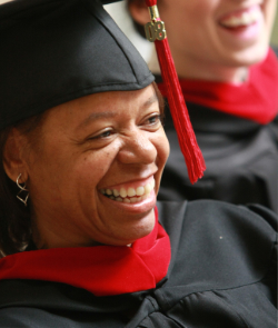 A graduate wearing a cap and gown smiles