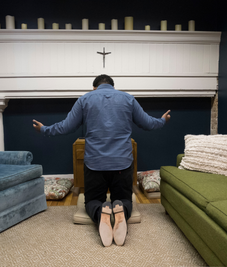 A theology student kneels in front of a cross.