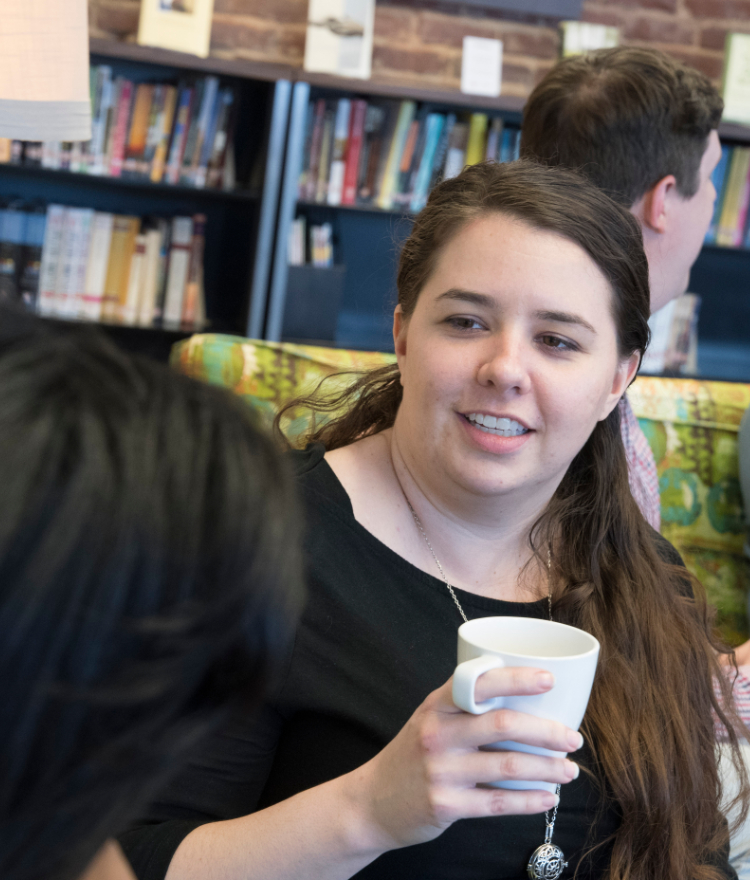 A theology student holds a coffee cup while chatting with another student.