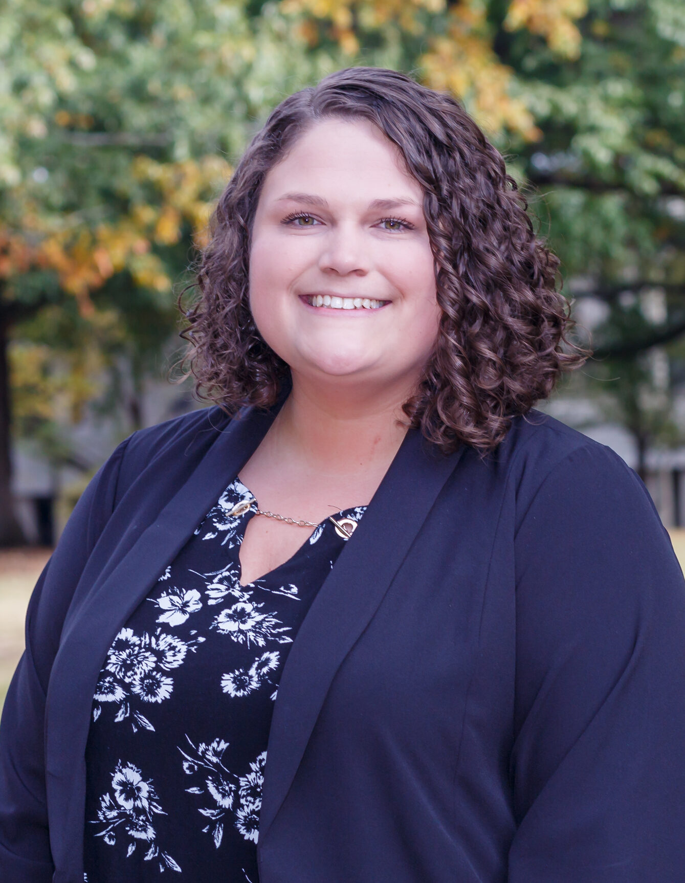 Megan Currie - white female wearing flowered blouse and black blazer