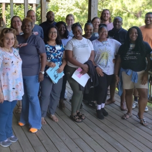 a large group of students, staff, and faculty on a porch overlooking the woods