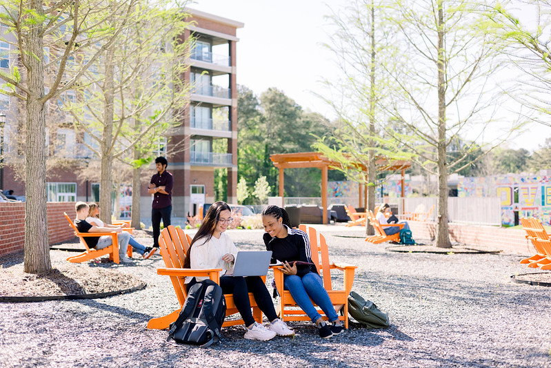 Two women sitting in orange adirondack chairs outside