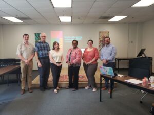 Three students with their mentors and the program director posing in a classroom. 