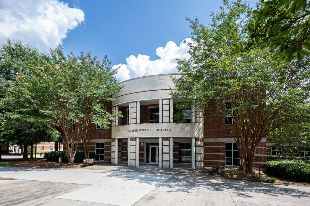 Brick and concrete building entrance with trees on each side and a sidewalk