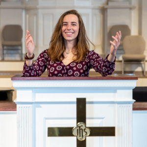 A white woman with her arms raised behind a pulpit