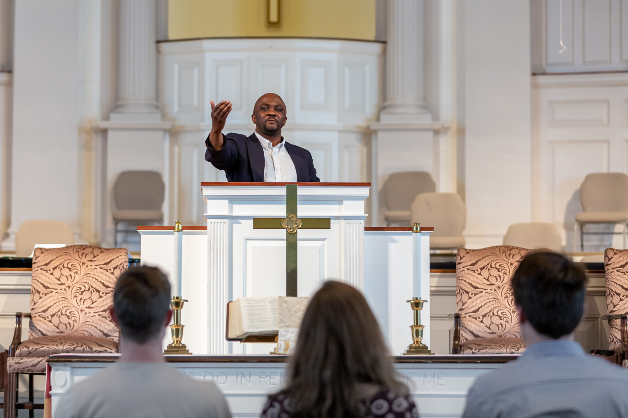 A black man behind a pulpit motioning to the audience