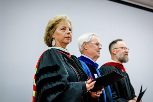 One woman and two men standing in academic regalia