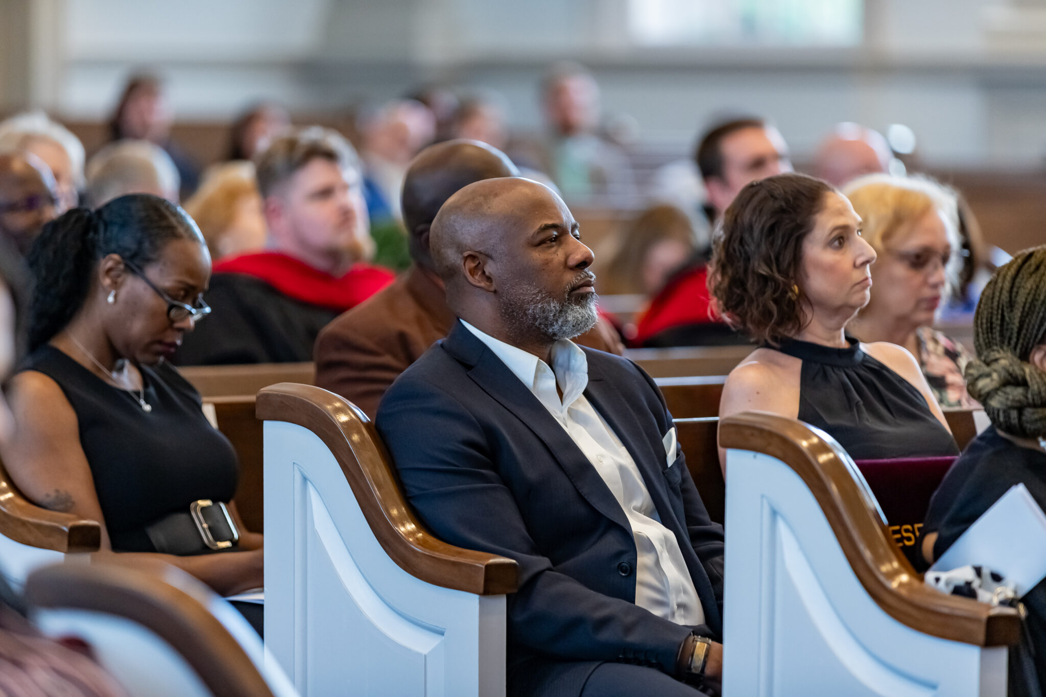 Black male and white female sitting on a pew with other students listening to a speaker