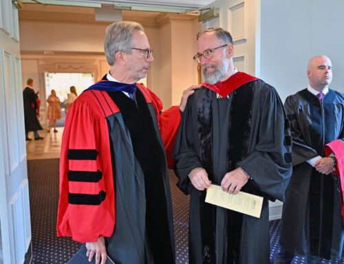 Two white me talking, wearing academic regalia